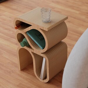 May include: A wooden side table with a unique, curved design. The table has multiple shelves and compartments for storage. A glass cup and a book are on the top shelf.