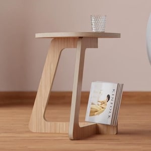 Peut inclure: Un canap&eacute; gris clair arrondi avec une base en bois se trouve &agrave; c&ocirc;t&eacute; d'une petite table d'appoint en bois avec un magazine sur l'&eacute;tag&egrave;re. Un verre transparent se trouve sur le dessus de la table.
