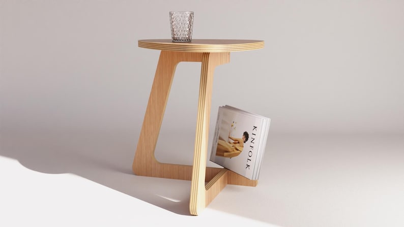 Peut inclure: Une table d'appoint en bois clair avec un plateau rond et un porte-revues en dessous. La table a un design unique et angulaire et est faite de contreplaqu&eacute;.