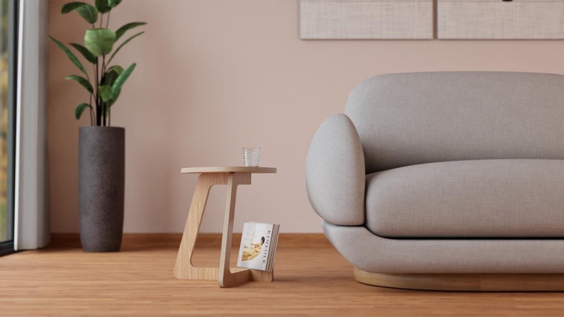 Peut inclure: Un canap&eacute; gris clair arrondi avec une base en bois se trouve &agrave; c&ocirc;t&eacute; d'une petite table d'appoint en bois avec un magazine sur l'&eacute;tag&egrave;re. Un verre transparent se trouve sur le dessus de la table.