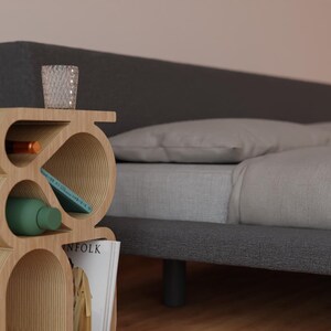 May include: A wooden bedside table with a unique, curved design. The table has multiple shelves and compartments for storage. It is next to a gray bed with white bedding.