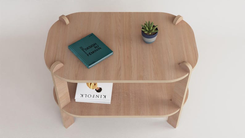 Puede incluir: Una mesa de centro de madera clara con un estante inferior. Un libro turquesa con el texto "DESIGN AU FEMININ" y una peque&ntilde;a planta en maceta est&aacute;n sobre la mesa. Una copia de "KINFOLK" est&aacute; en el estante inferior.