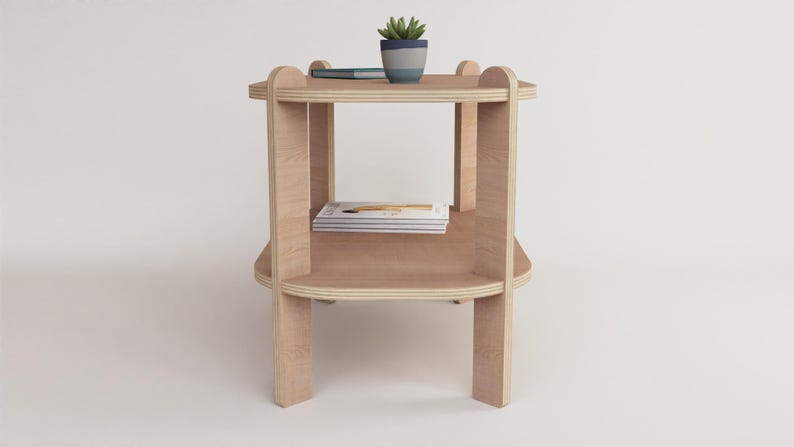 Puede incluir: Una mesa auxiliar de madera clara con dos estantes y esquinas redondeadas. Una peque&ntilde;a planta en maceta y un bol&iacute;grafo descansan sobre el estante superior. La mesa mide aproximadamente 61 cm de altura.