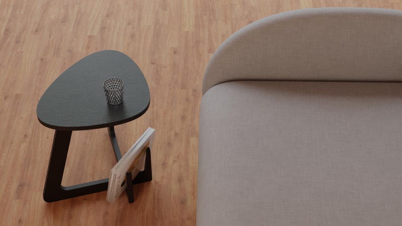 Peut inclure: Une table d'appoint triangulaire noire avec un porte-revues et un petit panier en fil de fer sur le dessus. La table est &agrave; c&ocirc;t&eacute; d'un canap&eacute; gris clair.
