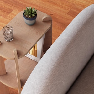 May include: A light wood side table with a small succulent in a blue and white pot, and a decorative glass. The table has a lower shelf and is next to a gray sofa. The table is approximately 20 inches long.