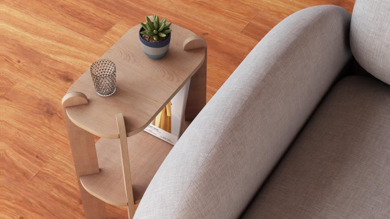 May include: A light wood side table with a small succulent in a blue and white pot, and a decorative glass. The table has a lower shelf and is next to a gray sofa. The table is approximately 20 inches long.