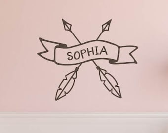 Könnte beinhalten: Ein weißes Babybett mit einem rosa-schwarzen Polka-Dot-Bettrock und Bettwäsche. Ein Wandtattoo über dem Babybett zeigt den Namen "Sophia" auf einem Banner mit Pfeilen und Federn. Eine passende Polka-Dot-Truhe und Lampe befinden sich ebenfalls im Raum.