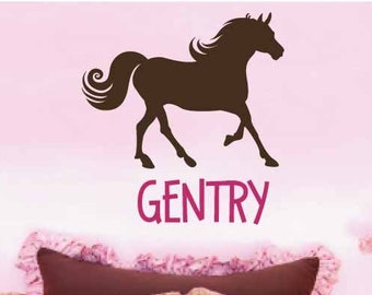 Könnte beinhalten: Ein rosa Schlafzimmer mit einer braunen Pferdesilhouette über einem Bett. Das Bett hat rosa und weiß gestreifte Kissen, ein rundes Kissen mit Punkten und eine rosa Bettdecke mit Punkten. Der Name "GENTRY" steht darunter.