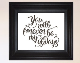Könnte beinhalten: Ein schwarzer gerahmter Druck mit dem Text "You will forever be my always" auf weißem Hintergrund. Der Druck hängt an einer weißen Wand über einem Bett mit weißen Bettwäsche und rosa und pfirsichfarbenen Kissen.
