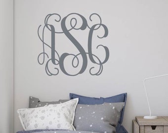 Könnte beinhalten: Ein graues Monogramm-Wandtattoo über einem Bett mit blauer und weißer Bettwäsche. Rechts befindet sich ein weißer Schreibtisch mit Lampe und Stuhl. Der Raum hat ein modernes, minimalistisches Design.