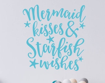Könnte beinhalten: Ein Wandtattoo mit dem Schriftzug "Mermaid kisses & Starfish wishes" in türkisfarbener Schrift, verziert mit Sternen. Darunter befindet sich ein Drahtkorb mit dekorativen Kugeln in verschiedenen Farben. Das Thema ist maritim und verspielt.