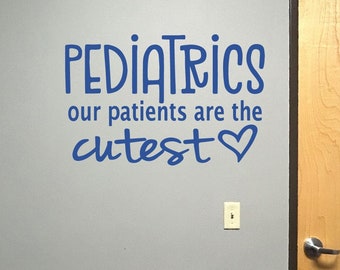 Könnte beinhalten: Blauer Wandaufkleber mit dem Wort "PEDIATRICS" über dem Satz "our patients are the cutest" und einem Herzsymbol. Der Aufkleber befindet sich an einer grauen Wand neben einer Holztür.