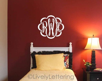 Könnte beinhalten: Ein weißes Monogramm mit den Buchstaben RWB in einem floralen Design ist an einer tiefroten Wand angebracht. Das Monogramm befindet sich über einem Bett mit einer gelben Bettdecke und einem Kissen. Ein Nachttisch und eine Lampe sind ebenfalls zu sehen.