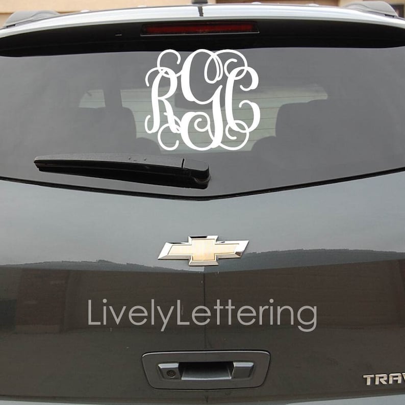 K&ouml;nnte beinhalten: Ein wei&szlig;er Monogramm-Aufkleber mit den Buchstaben "RGC" in einer kursivschriftlichen Schriftart, angebracht an der Heckscheibe eines grauen Autos. Das Auto hat ein goldenes Chevrolet-Emblem am Heck.