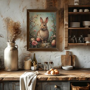 May include: A framed painting of a brown rabbit sitting on a rock surrounded by flowers and Easter eggs. The painting is in a rustic kitchen setting with a wooden shelf and a wooden countertop.