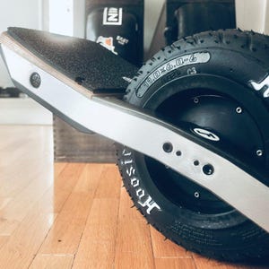 Könnte beinhalten: Ein silbernes und schwarzes Elektro-Skateboard mit einem schwarzen Reifen, auf dem "Hoosier" in weißen Buchstaben steht. Der Reifen hat die Größe 10,0x6,0-6.