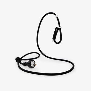 May include: A black electrical cord with a three-prong plug and a loop design. The cord has a white clip and a coiled section near the top, creating a modern and minimalist aesthetic. The cord is designed for electrical use.