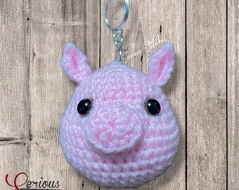May include: A handmade pink crochet pig keychain with black safety eyes and a silver keyring. The pig has a rounded snout and upright ears. The text "Serious Stitches" is visible in the lower left corner.