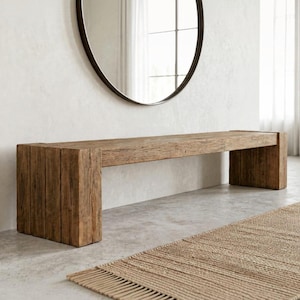 May include: A rectangular bench constructed from reclaimed wood with a visible grain and weathered texture. The bench features thick, block-style legs on both ends and a flat, horizontal seat surface, showcasing a natural brown finish.
