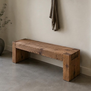 May include: A rectangular wooden bench constructed from thick, reclaimed timber planks with visible grain patterns and knots. The bench features a sturdy, block-style leg design at each end, showcasing a natural, weathered brown finish throughout.