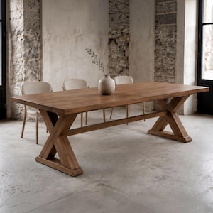 May include: A rectangular wooden dining table featuring a thick tabletop and a sturdy X-shaped trestle base. The table is crafted from medium-toned wood with a visible grain pattern. Three light-colored chairs are positioned along the side.