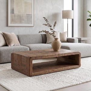 May include: A rectangular coffee table crafted from dark brown reclaimed wood with a smooth, low-profile design featuring an open centre shelf for storage. The table has a visible wood grain texture and a sturdy, block-like construction.