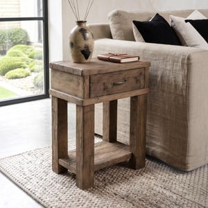 May include: A rectangular wooden side table with a natural brown finish, featuring a single drawer with a dark metal handle and a lower shelf. The table has a thick, sturdy frame with visible wood grain texture and a rustic, weathered appearance.