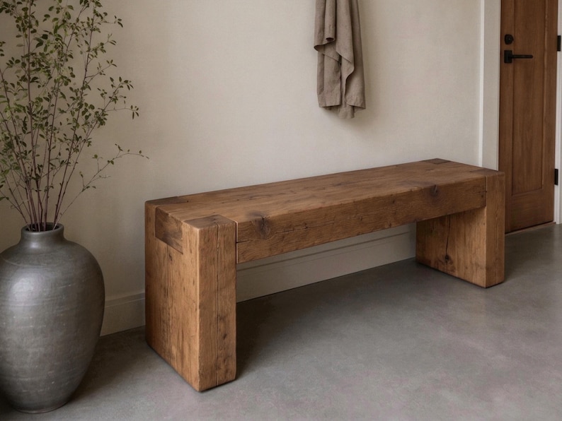 May include: A rectangular wooden bench constructed from thick, solid timber planks with a natural brown finish. The bench features a simple, block-style design with four sturdy legs integrated into the frame, showcasing a visible wood grain texture.