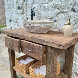 May include: A rustic wooden vanity with two drawers and a lower shelf. The vanity has a stone sink with a faucet and two soap dispensers.