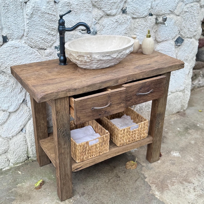 May include: A rustic wooden bathroom vanity with two drawers and a lower shelf. The vanity features a stone sink and a black faucet. Two woven baskets are on the shelf.