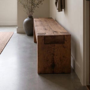 May include: A rectangular bench constructed from thick, dark brown reclaimed wood with a visible grain pattern. The bench features a sturdy, block-like design with prominent joinery details at the corners where the legs meet the seat surface.