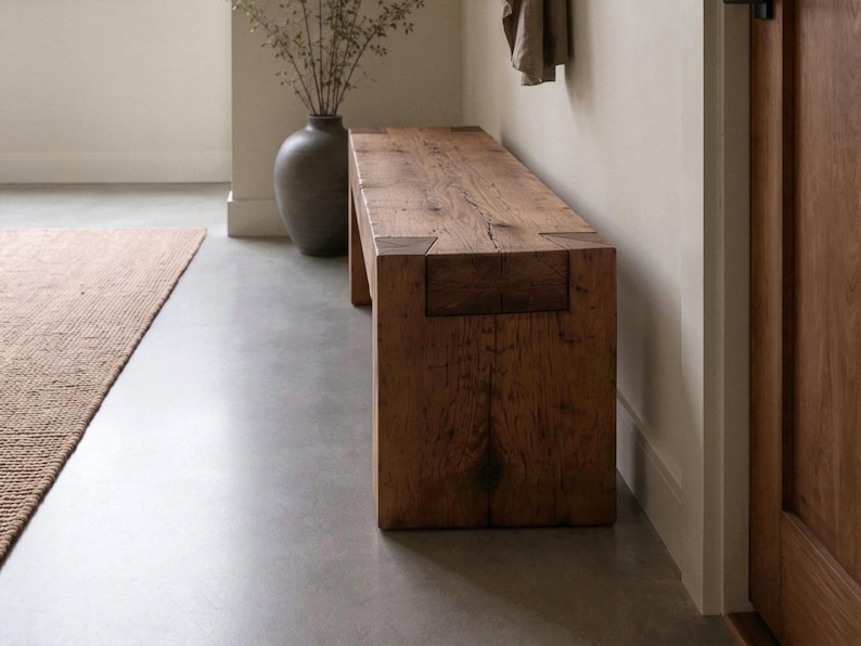 May include: A rectangular bench constructed from thick, dark brown reclaimed wood with a visible grain pattern. The bench features a sturdy, block-like design with prominent joinery details at the corners where the legs meet the seat surface.
