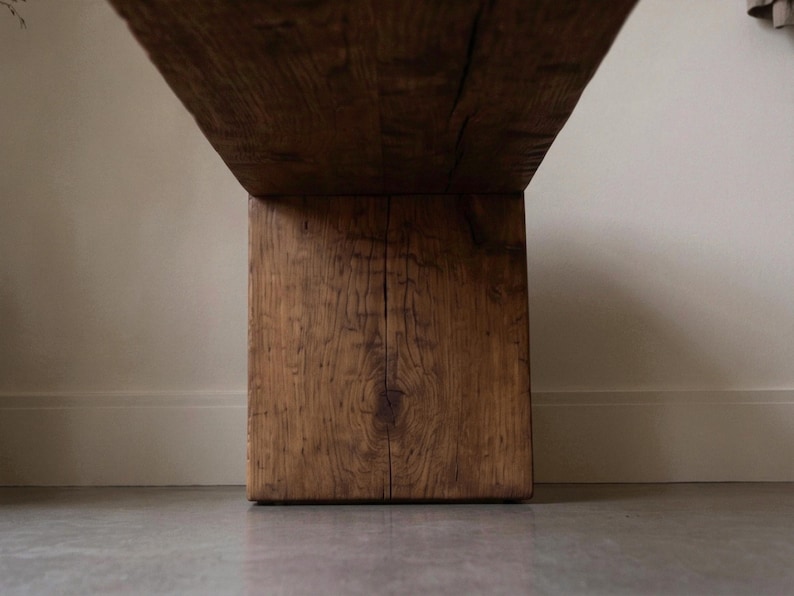 May include: A low-angle view of a heavy wooden bench featuring a thick, rectangular support leg and a wide, flat seat. The wood displays a deep brown tone with a prominent, natural grain pattern, visible knots, and a vertical crack running down the centre.