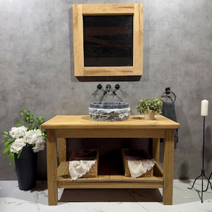 May include: A rustic wooden bathroom vanity with a stone sink, two woven baskets, and a framed mirror above. The vanity has a shelf and is made of reclaimed wood.