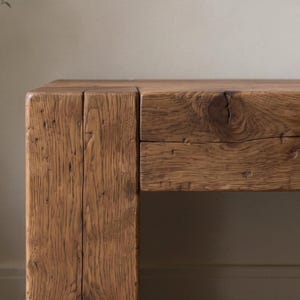 May include: A rectangular wooden table featuring a thick, block-style leg and a horizontal tabletop. The wood displays a natural medium-brown tone with visible grain patterns, deep vertical fissures, and a prominent knot on the front surface.