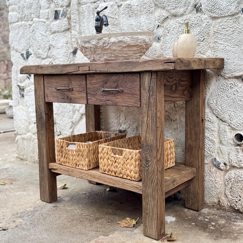 May include: Rustic wooden bathroom vanity with two drawers and a shelf. The vanity has a distressed brown finish and features a white porcelain sink and two woven baskets.