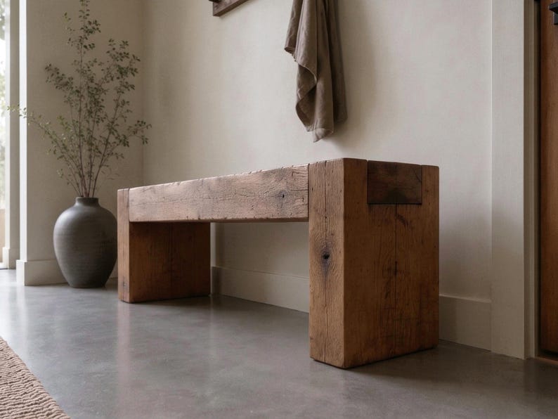 May include: A rectangular bench constructed from thick, reclaimed brown timber. The piece features a solid, block-style design with a flat seat and two sturdy, vertical support legs at each end, showcasing a natural wood grain and weathered texture.