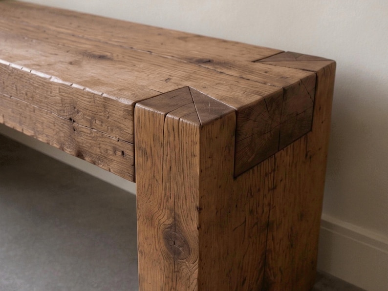 May include: A rectangular bench constructed from thick, reclaimed brown timber. The piece features visible wood grain, natural knots, and a sturdy joinery design where the horizontal seat meets the vertical leg with a flush, interlocking corner.