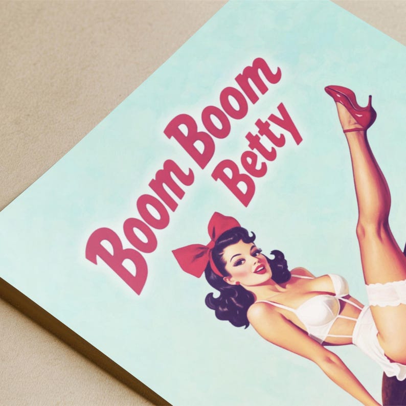 May include: A vintage-style print featuring a pin-up girl in white lingerie and a red bow, with the text "Boom Boom Betty" in pink. The artwork has a retro aesthetic with a light blue background.