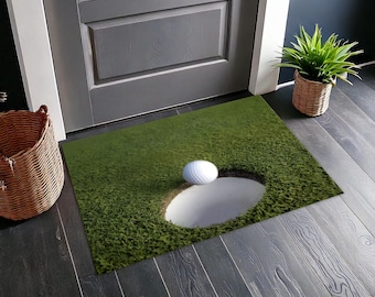 May include: A green golf course doormat with a white golf ball rolling into a sand trap.
