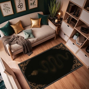 Könnte beinhalten: Ein schwarzer rechteckiger Teppich mit einem goldenen Schlangenmuster und einem verzierten goldenen Rand. Der Teppich liegt auf einem Holzboden in einem Raum mit Sofa, Kissen und Bücherregal. Der Teppich ist ca. 152 cm lang und 91 cm breit.