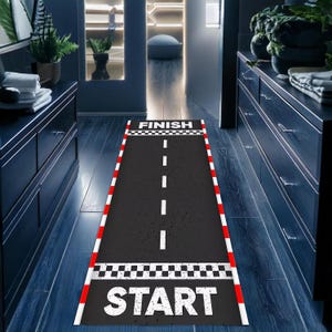Puede incluir: Una alfombra de pista de carreras en blanco y negro con bordes rojos. La alfombra tiene las palabras "FINISH" y "START" impresas en ella.