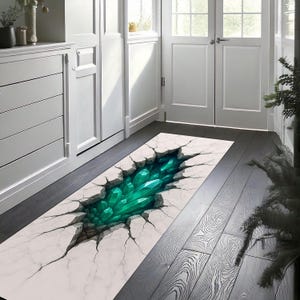 Può includere: Un tappeto rettangolare con un design 3D di una superficie incrinata che rivela un gruppo di cristalli verde smeraldo. Il tappeto ha un aspetto bianco marmoreo con crepe scure, creando un'illusione di profondità e consistenza. Il tappeto è posto su un pavimento in legno scuro.