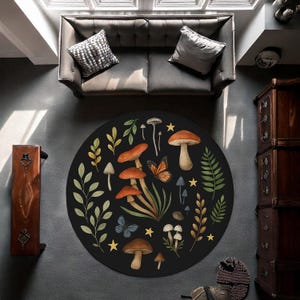 May include: A circular black rug with a nature-inspired design. The rug showcases illustrations of mushrooms, butterflies, and leaves in shades of orange, brown, green, and yellow. The rug is placed on a grey floor, with a grey sofa and cushions visible in the background.