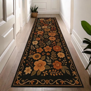 Può includere: Un lungo tappeto runner rettangolare a motivi floreali con sfondo nero e bordo. Il tappeto presenta un motivo ripetuto di fiori e foglie arancioni, gialle e verdi. Il bordo è color oro.