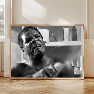 A black and white photograph of a man with a serious expression, appearing to be in a bathroom setting.