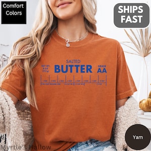 A woman wearing an orange t-shirt with a graphic design of a salted butter recipe.