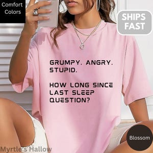 A person wearing a pink t-shirt with text printed on it, posing for a photo.