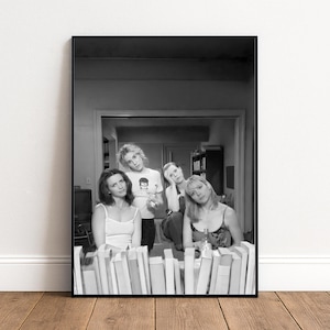 A black and white photograph of four people posing together in a room with bookshelves in the background.