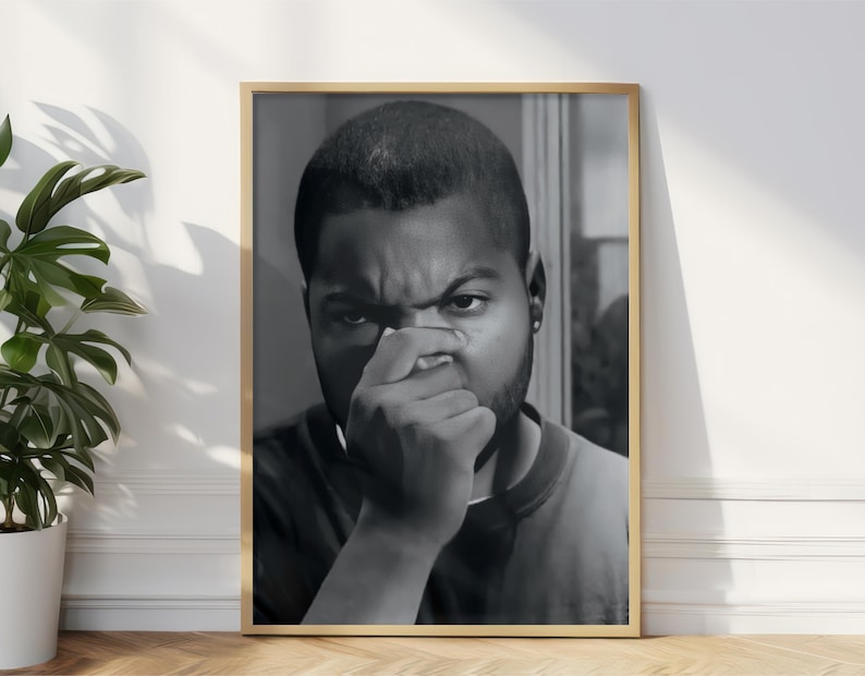 a framed black and white photograph of a man with a pensive expression, standing in front of a white wall.